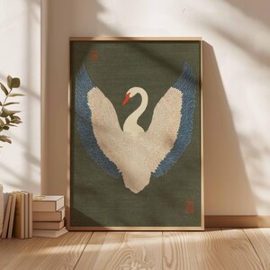 Pode incluir: Obra de arte emoldurada com um cisne com as asas abertas. O cisne tem penas brancas, um bico vermelho e pontas das asas azuis. O fundo &eacute; verde suave e a moldura &eacute; de madeira clara. A obra de arte tem um estilo art&iacute;stico tradicional.