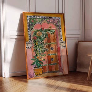 May include: A watercolor painting of a pink and yellow doorway with a green plant and flowers in a terracotta pot. The door is brown with green and blue details. The painting is framed in a wooden frame.