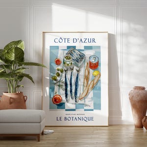 May include: A framed art print featuring a still life of sardines, olives, and bread on a blue and white checkered tablecloth. The print includes the text "C&Ocirc;TE D'AZUR" and "LE BOTANIQUE". The artwork has a vintage aesthetic.