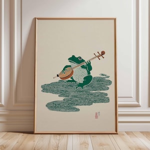 Peut inclure: Impression encadrée d'une grenouille verte jouant d'un instrument à cordes. La grenouille, avec des taches blanches, est posée sur des motifs d'eau verte. L'œuvre a une esthétique japonaise traditionnelle.