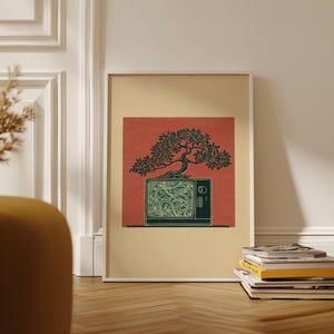 May include: Framed art print depicting a green bonsai tree on a vintage television. The TV screen shows a detailed green pattern against a red backdrop. The artwork is in a white frame, with books stacked on the floor.