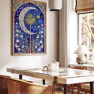 May include: A framed watercolor print featuring a crescent moon, palm tree, and floral elements against a deep blue background. The artwork has a gold frame and is displayed in a dining room setting with a glass-topped table and rattan chairs.