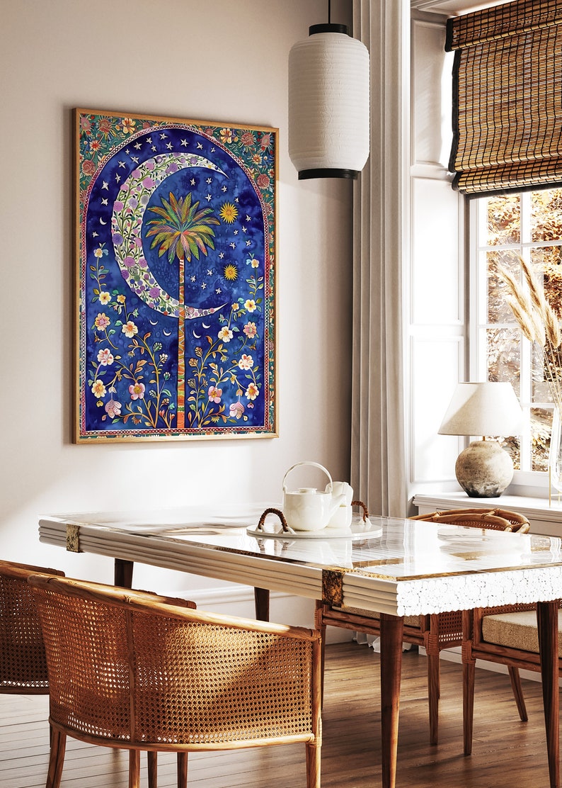 May include: A framed watercolor print featuring a crescent moon, palm tree, and floral elements against a deep blue background. The artwork has a gold frame and is displayed in a dining room setting with a glass-topped table and rattan chairs.