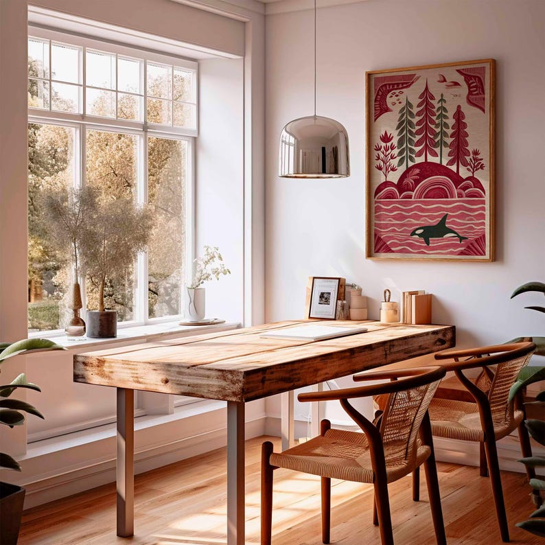 May include: A wooden desk with metal legs and two woven chairs sits in front of a large window. A framed art print depicting an orca in the ocean hangs on the wall. A silver pendant light hangs above the desk.