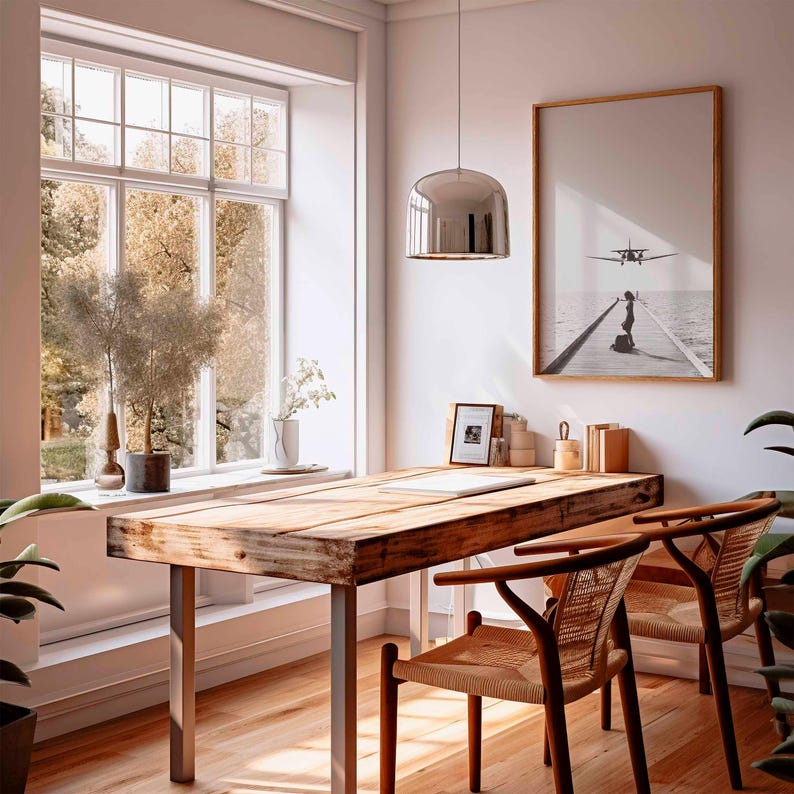 Puede incluir: Una oficina en casa con un escritorio de madera y dos sillas. Una foto en blanco y negro enmarcada cuelga de la pared. Una gran ventana ofrece vistas a los &aacute;rboles. Una l&aacute;mpara colgante plateada cuelga sobre el escritorio.