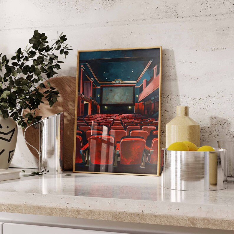 May include: A framed print of a movie theater interior with red seats and a large screen. The print is on a white countertop with a silver pitcher and a bowl of lemons.