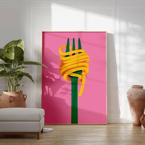 Op de afbeelding: Een ingelijste kunstdruk met een groene vork met gele spaghetti op een roze achtergrond. Het kunstwerk wordt getoond in een kamer met een grote potplant, een grijze poef en decoratief aardewerk. Het thema is eten en kunst.
