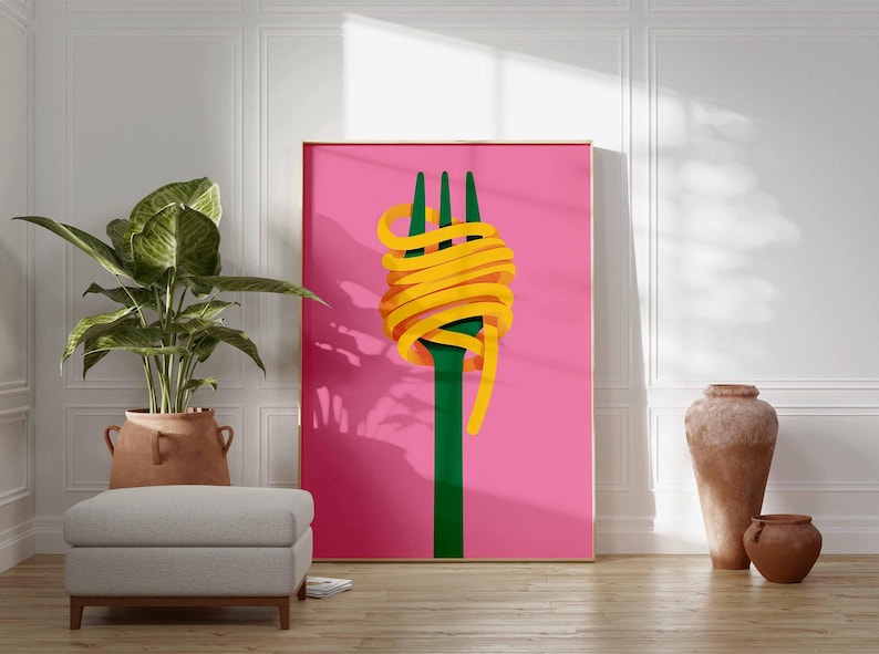 Op de afbeelding: Een ingelijste kunstdruk met een groene vork met gele spaghetti op een roze achtergrond. Het kunstwerk wordt getoond in een kamer met een grote potplant, een grijze poef en decoratief aardewerk. Het thema is eten en kunst.