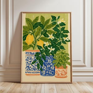 May include: A framed art print featuring a botanical illustration of two lemon trees and a small herb plant in decorative pots. The pots have blue and white patterns, and the plants have green leaves, yellow lemons, and white flowers.