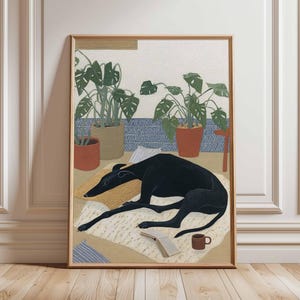 May include: A framed art print depicts a black dog lounging on a rug with a book and a mug. Potted plants and patterned pillows are in the background. The artwork is in a wooden frame and has a neutral color palette.