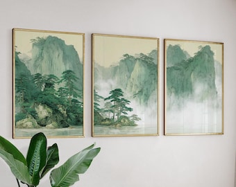 May include: Three framed landscape art prints. Each print features a mountain scene with green and teal hues, trees, and a misty atmosphere. The frames are gold-colored, and the artwork is displayed on a white wall.