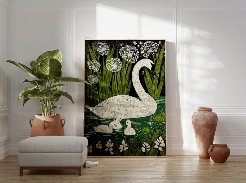 May include: A framed art print featuring a white swan with two cygnets swimming in a pond, surrounded by green foliage and white dandelions. The artwork has a black background and is displayed in a room with a plant, ottoman, and decorative vases.