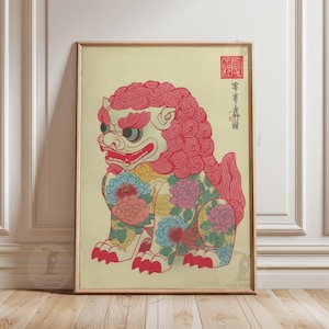 May include: Framed print of a colorful Foo Dog, a traditional guardian lion. The artwork features a red mane, floral patterns, and Japanese text. The print is in a gold frame and is displayed against a cream-colored background.