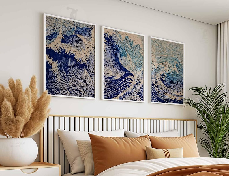 May include: Three framed art prints depicting stylized ocean waves in shades of blue and beige. The artwork is displayed above a bed with orange and white bedding. The prints are in white frames.