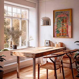 May include: A wooden table with a light wood finish and a metal frame. The table has a white painted surface and is decorated with a painting of a colorful door with flowers. Two wicker chairs are placed at the table.