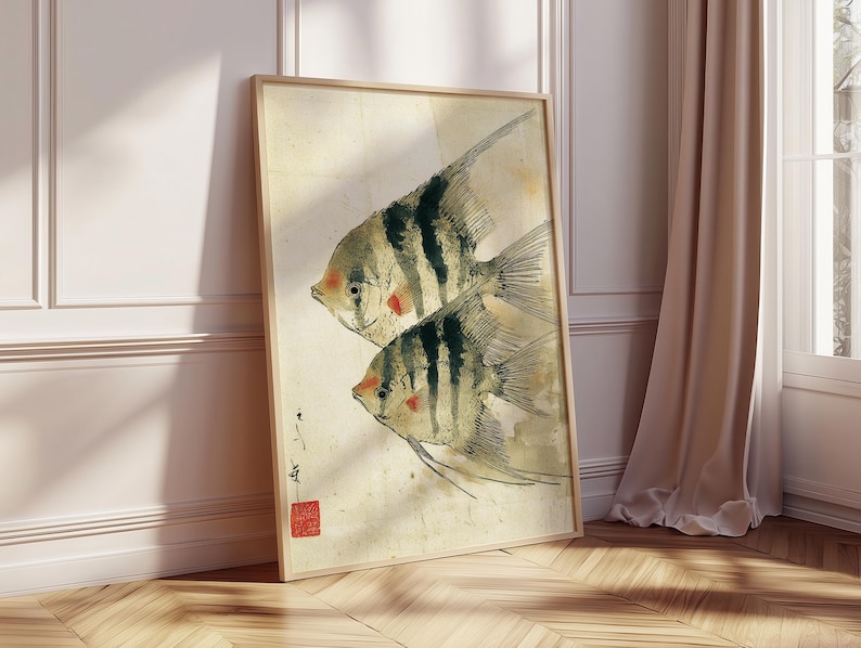 K&ouml;nnte beinhalten: Gerahmter Kunstdruck mit zwei stilisierten Fischen mit schwarz-wei&szlig;en Streifen und roten Akzenten. Das Kunstwerk hat eine Vintage-&Auml;sthetik mit beigem Hintergrund und Holzrahmen. Der Druck lehnt an einer Wand und einem Fenster.