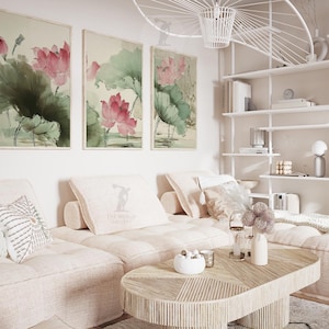 May include: Three framed watercolor paintings of lotus flowers in shades of pink and green hang above a light-colored sectional sofa. A wooden coffee table and decorative pillows complete the living room setting.