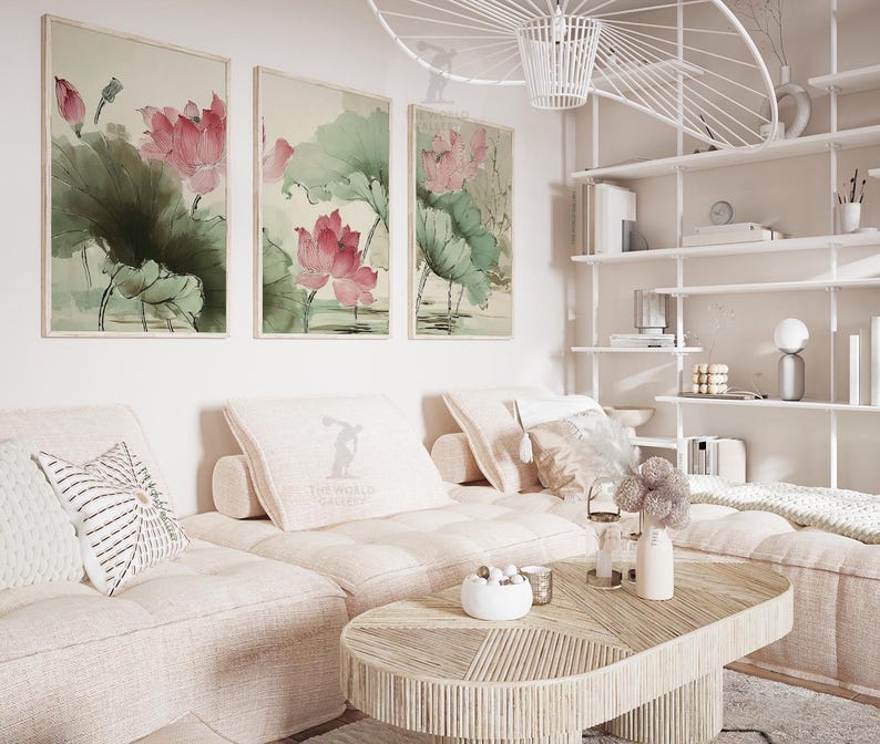 May include: Three framed watercolor paintings of lotus flowers in shades of pink and green hang above a light-colored sectional sofa. A wooden coffee table and decorative pillows complete the living room setting.