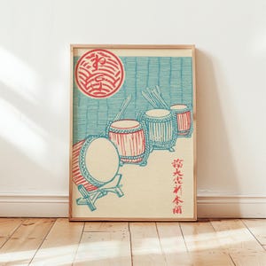 May include: A framed print featuring a traditional Japanese design. The artwork depicts three red and blue drums with drumsticks, set against a blue background with a red circular emblem. Japanese text is also present.