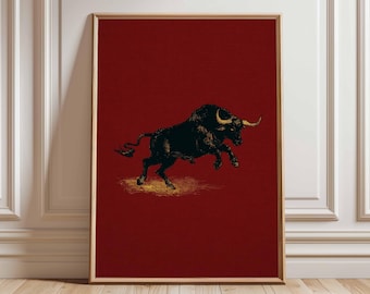 May include: Framed art print featuring a black bull with golden horns, set against a deep red background. The bull is depicted in a dynamic pose, with its front legs raised. The artwork is framed in a simple, light-colored wooden frame.