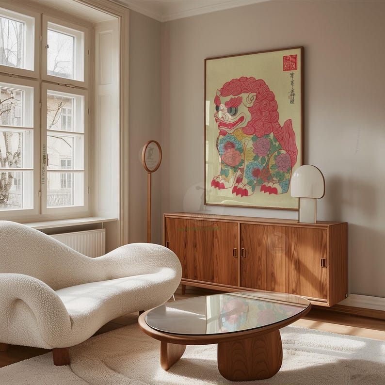 May include: A living room scene featuring a large framed artwork of a colorful, stylized lion. The artwork hangs above a wooden cabinet. A white, curved sofa and a round coffee table with a glass top are in the foreground. A white lamp and a decorative mirror are also visible.