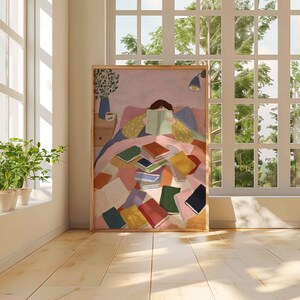 May include: A framed art print depicts a person reading in bed, surrounded by colorful books. The artwork is set against a window with natural light and potted plants. The room has a wooden floor.