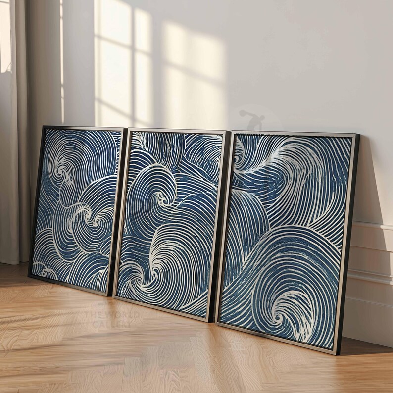 May include: Three framed abstract art pieces. Each features a swirling pattern of white lines on a dark blue background. The frames are black with a silver inner border. The artwork leans against a white wall on a wooden floor.