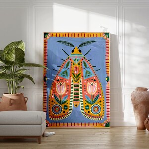 Pode incluir: Uma grande pintura colorida de uma mariposa com fundo azul. A mariposa tem padr&otilde;es intrincados em laranja, amarelo e azul-petr&oacute;leo. A pintura &eacute; emoldurada em uma borda amarela e vermelha. Uma planta em vaso, um pufe e vasos est&atilde;o em primeiro plano.
