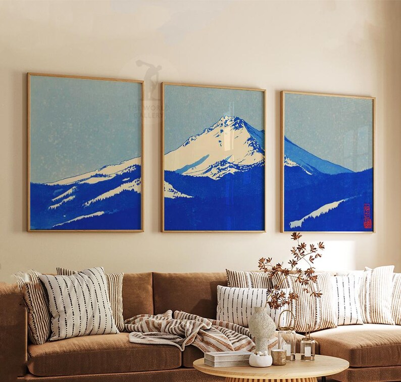 K&ouml;nnte beinhalten: Drei gerahmte Kunstdrucke, die eine Bergkette in Blau- und Wei&szlig;t&ouml;nen darstellen. Das Kunstwerk hat eine japanische &Auml;sthetik, mit einem hellblauen Himmel und einem schneebedeckten Berggipfel. Die Rahmen sind hellholzfarben.
