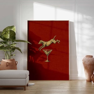 Pu&ograve; includere: Una stampa artistica incorniciata con un cane dorato che salta sopra un bicchiere da cocktail dorato su sfondo rosso. L'opera d'arte &egrave; esposta in una stanza con una grande pianta in vaso, un pouf grigio e ceramiche decorative.