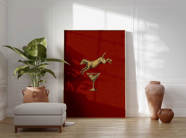 Pu&ograve; includere: Una stampa artistica incorniciata con un cane dorato che salta sopra un bicchiere da cocktail dorato su sfondo rosso. L'opera d'arte &egrave; esposta in una stanza con una grande pianta in vaso, un pouf grigio e ceramiche decorative.