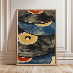 May include: A framed art print featuring a stack of vintage vinyl records. The records are primarily black and blue, with yellow and red center labels. The artwork has a retro, graphic style, and is displayed in a wooden frame.