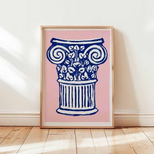 May include: A framed print depicting a blue and white illustration of a classical column on a pink backdrop. The column's capital features scroll and floral details. The artwork is presented within a wooden frame, suitable for interior decor.