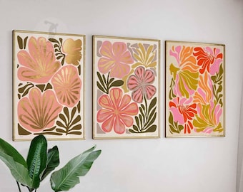 May include: Three abstract floral prints in a set. The prints feature pink, red, and orange flowers with gold accents on a white background. The prints are framed in gold.