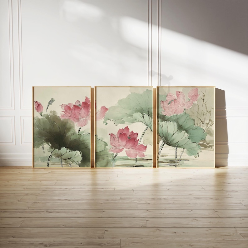 May include: Three framed art prints featuring watercolor paintings of pink lotus flowers and large green leaves. The artwork has a traditional Asian style, with gold frames and a neutral background. The prints are displayed on a wooden floor.