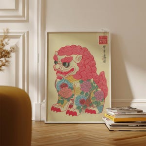 May include: Framed art print featuring a stylized, colorful lion-like creature with floral patterns. The artwork has a red mane, red paws, and a red mouth. The background is a light yellow color.