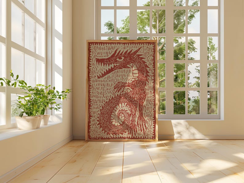 May include: A framed artwork featuring a red dragon illustration. The dragon is depicted with sharp teeth and a long tail, set against a textured, off-white background. The artwork is displayed in a room with natural light.