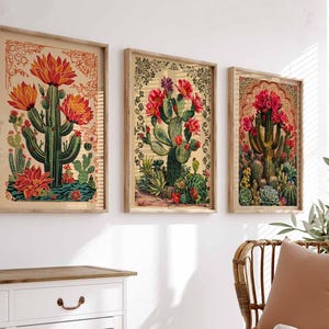 May include: Three framed botanical prints featuring cacti with red flowers and green leaves on a beige background. The prints are in wooden frames with a light brown finish.