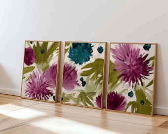 May include: Three framed floral art prints. Each print features abstract flowers in shades of purple, teal, and green against a cream background. The frames are a light wood color, and the artwork is displayed on a white wall.