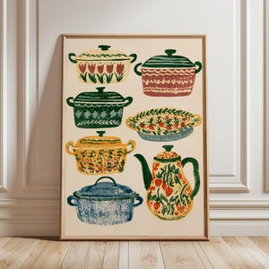 May include: A framed wall art print featuring a collection of kitchenware illustrations on a cream background. The artwork displays four lidded pots, one shallow dish, and a teapot, each decorated with colourful floral, strawberry, and leaf patterns.