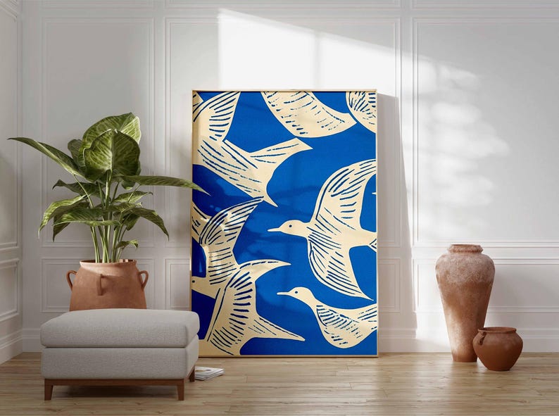 May include: A framed art print featuring a flock of birds in flight against a vibrant blue background. The birds are depicted in a cream color with detailed linework. The artwork is displayed in a room with a plant, ottoman, and decorative vases.