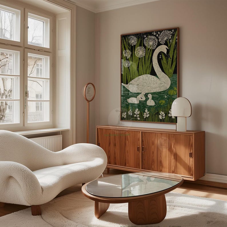 May include: A living room scene featuring a white, curved sofa, a wooden coffee table, and a wooden cabinet. A framed artwork of a swan and cygnets in a pond hangs on the wall. A white lamp and a round mirror complete the decor.