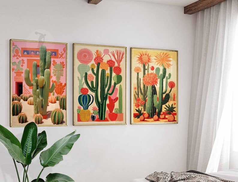 May include: Three framed prints of colorful cactus illustrations. The prints feature a variety of cacti in different colors and patterns, including green, red, orange, and yellow. The prints are set against a white wall.