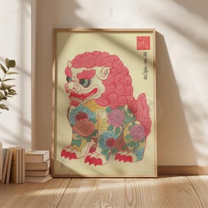 May include: Framed print of a stylized lion-dog with a red mane and floral patterns. The artwork features a light yellow background and is framed in natural wood. The lion-dog has a red mouth and green eyes. Japanese characters are visible in the upper right corner.