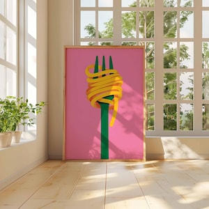 Op de afbeelding: Een ingelijste kunstprint met een groene vork met gele spaghetti op een roze achtergrond. Het kunstwerk staat in een kamer met een raam en planten.