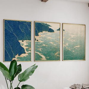 May include: Three framed art prints showing a coastal scene. The artwork uses a blue and green colour palette, with detailed illustrations of cliffs, ocean waves, and a serene seascape. The frames have a gold finish, adding a touch of elegance to the artwork.