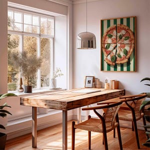 May include: A dining room scene featuring a wooden table with metal legs, two woven chairs, and a large window. A framed pizza art piece hangs on the wall. A silver pendant light hangs above the table. Plants and decor are on the windowsill.