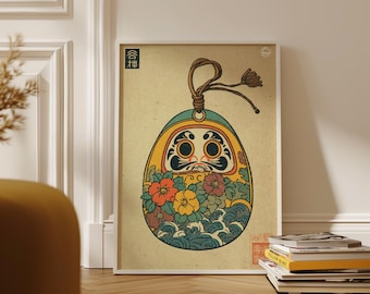 Könnte beinhalten: Gerahmter Kunstdruck einer Daruma-Puppe. Die Illustration zeigt eine gelbe Daruma-Puppe mit schwarzem Gesicht, floralen Details und blauen Wellen. Der Druck befindet sich in einem weißen Rahmen und liegt auf einem Holzboden.