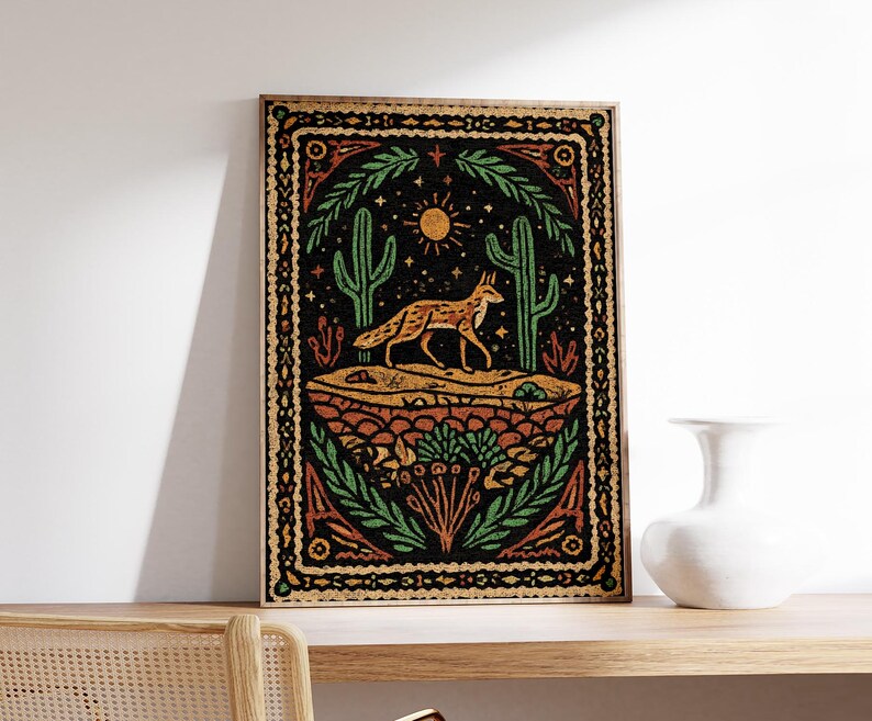 May include: A framed art print featuring a desert scene with a fox, cacti, and sun. The artwork has a black background with orange, green, and yellow accents. The print is displayed on a wooden shelf.