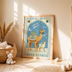 May include: A framed art print featuring a camel and a baby camel in a desert scene with a blue night sky, stars, and a crescent moon. The camel is tan with decorative saddlebags. The print is in a light wood frame.